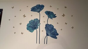 Eine Wand mit drei großen blauen Blumen und kleinen Schmetterlingsaufklebern.