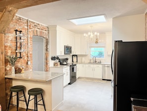 A kitchen with white cabinets, a black refrigerator, a built-in oven, and a window with a view of greenery.
