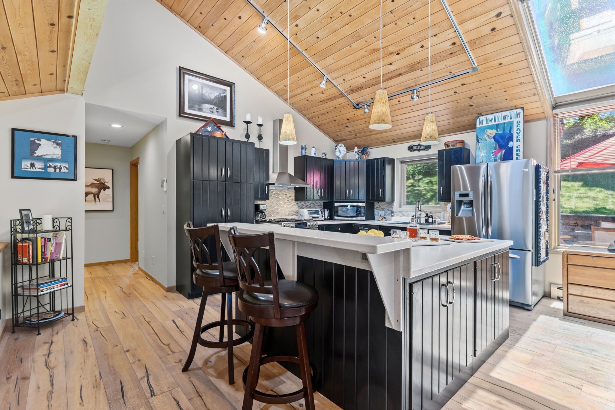 A modern kitchen with a central island, bar stools, and a large refrigerator.