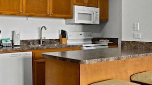 A kitchen with wooden cabinets, a microwave, a stove, a dishwasher, and granite countertops.