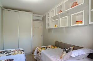 A bedroom with two single beds, a wardrobe, and a shelf with decorative items. - Luxury Penthouse in Jurerê Internacional: 150m² Terrace, Private Pool and Suite (Florianópolis)