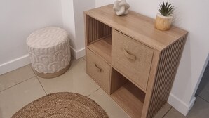 Een hoekje met een houten kast, een rond geweven vloerkleed en een klein rond krukje.