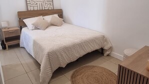 Een slaapkamer met een bed, een nachtkastje, een kunstwerk aan de muur, een rond geweven vloerkleed en een houten kast.