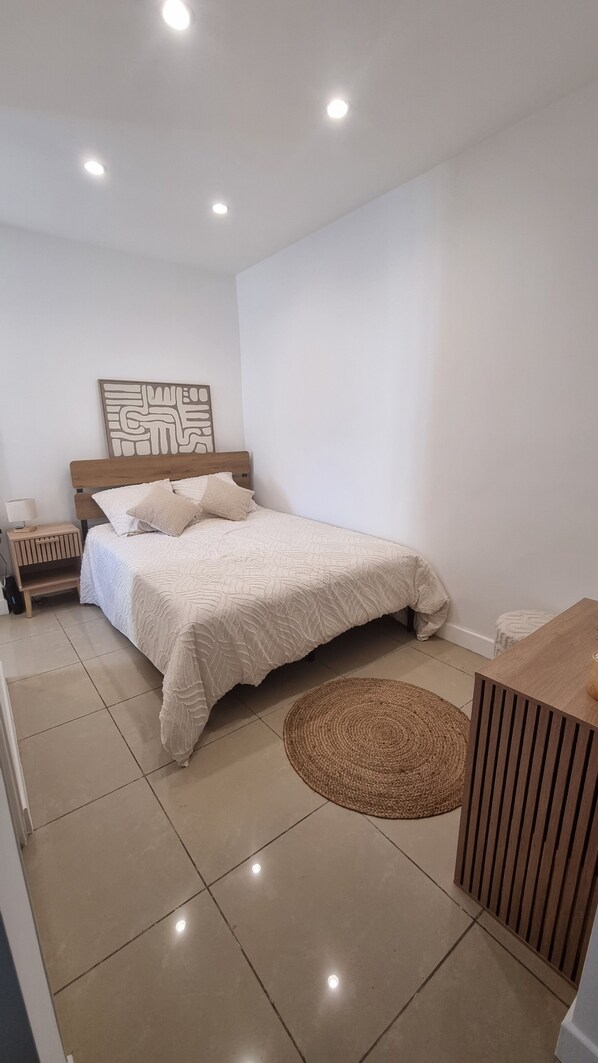 Ein Schlafzimmer mit einem Bett, einem Nachttisch, einem Wandbild, einem runden gewebten Teppich und einem Holzschrank.
