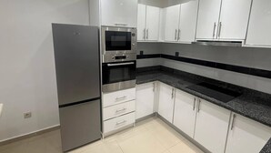 A modern kitchen with white cabinets, a stainless steel refrigerator, a built-in oven, and a microwave.