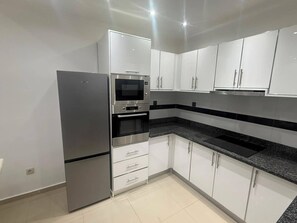 A modern kitchen with white cabinets, a stainless steel refrigerator, a built-in oven, and a microwave. - House Lima (Lobito)