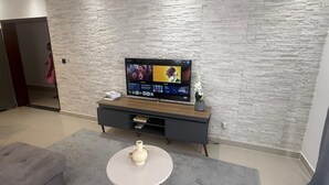 A modern living room with a stone-textured wall, a flat-screen TV, a grey sofa, a small round table with a vase, and a dark wooden entertainment unit.