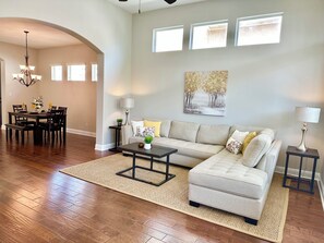 A spacious living room with hardwood flooring, a sectional sofa, a dining area with a table and chairs, and a chandelier. - Amazing upscale beautiful home near Lake Travis and panoramic hill country view. (Lakeway)
