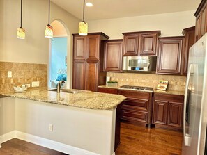 A kitchen with wooden cabinets, granite countertops, a stainless steel refrigerator, and a built-in microwave. - Amazing upscale beautiful home near Lake Travis and panoramic hill country view. (Lakeway)