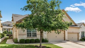 Una casa residencial con garaje, césped y un árbol en la parte delantera.