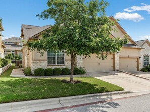A residential house with a garage, a lawn, and a tree in front. - Amazing upscale beautiful home near Lake Travis and panoramic hill country view. (Lakeway)