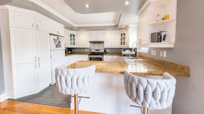 A modern kitchen with white cabinetry, granite countertops, and two bar stools.