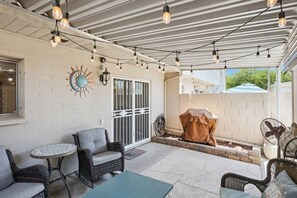 Eine Terrasse im Freien mit Korbmöbeln, Lichterketten und einem Grill.