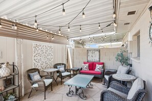 Une terrasse extérieure avec des meubles en osier, un canapé rouge et des guirlandes lumineuses.