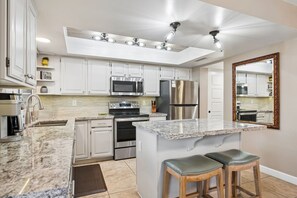 Eine moderne Küche mit weißen Schränken, Edelstahlgeräten, einer Granit Arbeitsplatte und einem Barhocker.