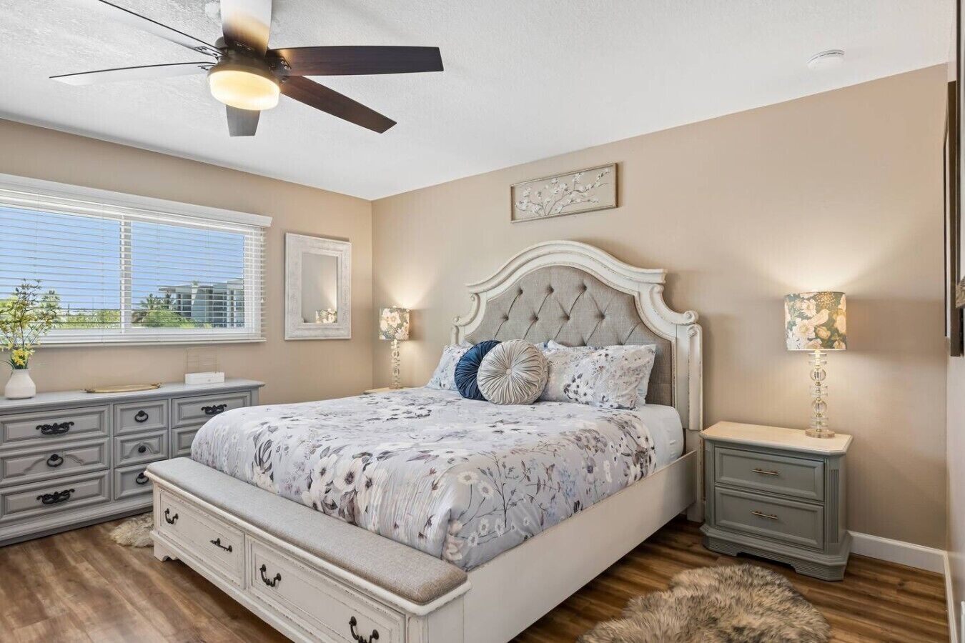 A bedroom with a bed, dresser, nightstands, a ceiling fan, and a window with blinds.