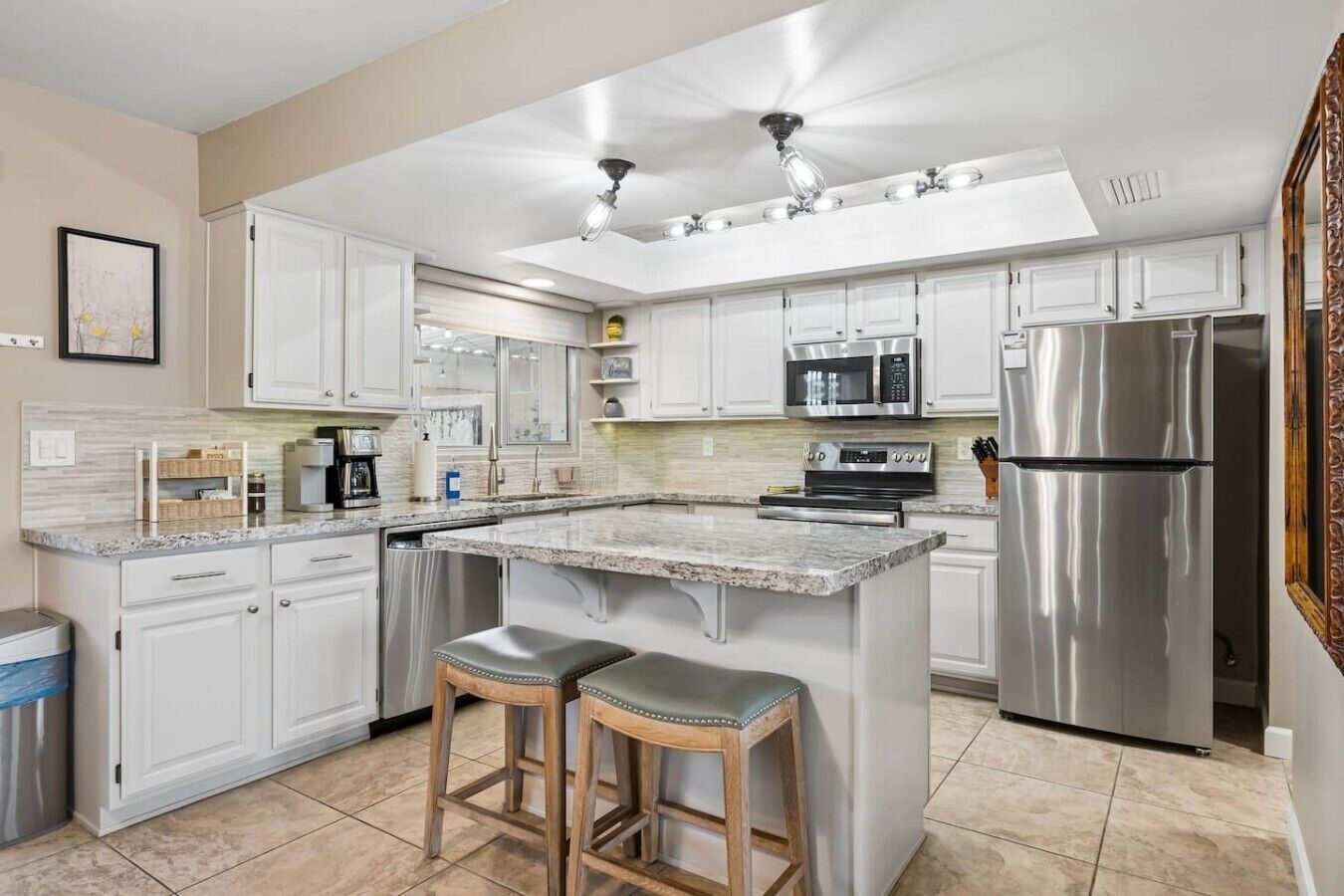 A modern kitchen with white cabinetry, stainless steel appliances, a granite countertop, and a central island with stools.