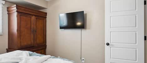 A bedroom with a bed, a wooden wardrobe, a television mounted on the wall, and a white door.