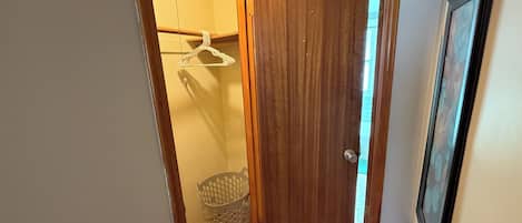 Un couloir avec une porte en bois, un panier à linge et un tableau encadré accroché au mur.