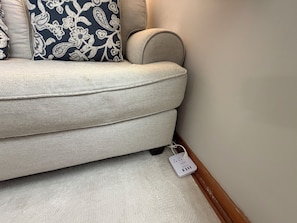 A beige sofa with a patterned pillow, a power strip on the floor, and a wooden baseboard. - Private apartment suite in Omaha! (Omaha)