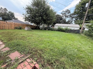 A residential backyard with a wooden fence, a tree, and a paved walkway.