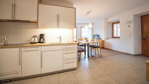 Una cocina moderna con armarios blancos, un comedor con mesa y sillas, y una sala de estar con televisor.