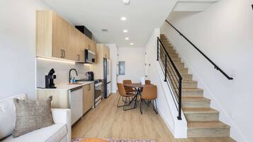 Una cocina moderna con armarios de madera, un comedor con mesa y sillas, una escalera y una pared blanca.