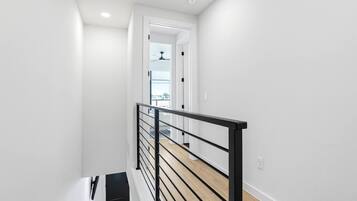 Una escalera moderna con barandilla negra, paredes blancas y piso de madera.