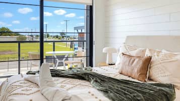 Habitación de hotel con un gran ventanal, una cama con una manta verde y vistas a un campo deportivo.