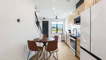 A modern kitchen with white cabinets, a dining area with brown chairs, and a view through the window.