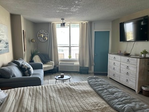 Ein Schlafzimmer mit einem Bett, einem Sofa, einem Schminktisch, einem Fernseher und einem Fenster mit Vorhängen.
