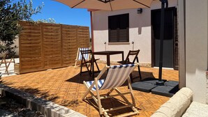 Un patio con una mesa, dos sillas, una silla reclinable a rayas y un paraguas grande.