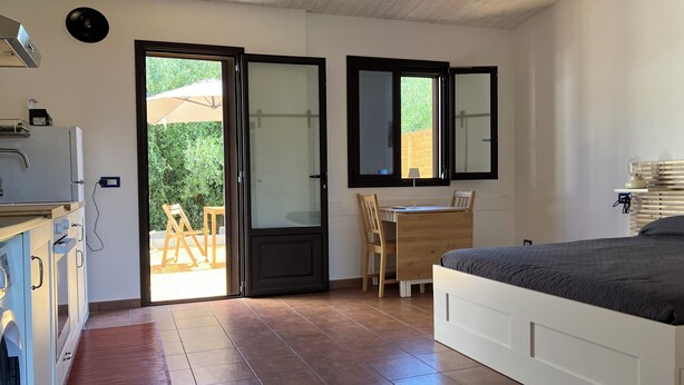 Un dormitorio con una cama, un escritorio y una silla. Se ve vegetación por la ventana.