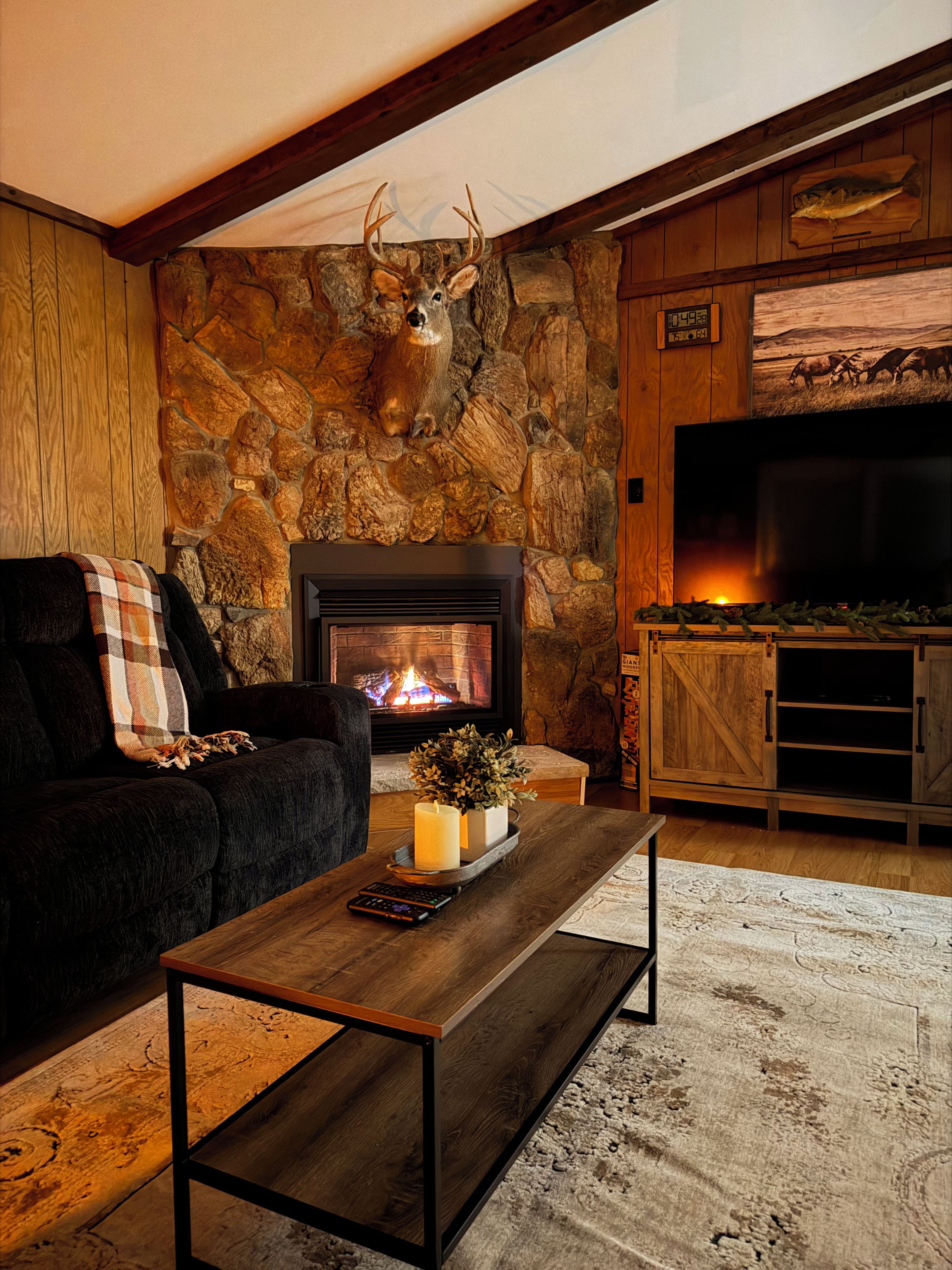 A cozy living room with a stone wall, a fireplace, a mounted deer head, and a television.