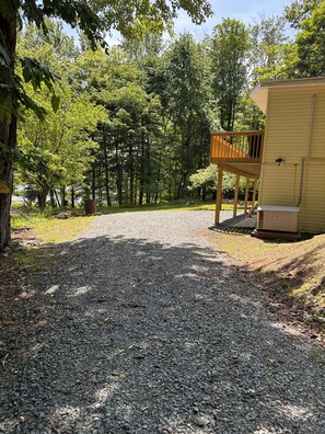 A gravel path leading to a wooden deck and a small building, surrounded by dense trees. - Cozy, relaxing,  3-bedroom home on lake Ponderosa with AC in serene Honesdale (Honesdale)