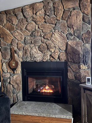 A stone fireplace with a fire, a clock, and a guitar on the wall. - Cozy, relaxing,  3-bedroom home on lake Ponderosa with AC in serene Honesdale (Honesdale)