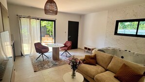A modern living room with a sofa, a coffee table, a dining table, and a hot tub. - The River's Cocoon (Saint-Drézéry)