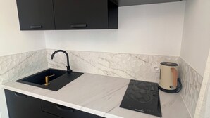 A modern kitchen with black cabinets, a marble countertop, a black sink, and a Valterra induction cooktop. - The River's Cocoon (Saint-Drézéry)