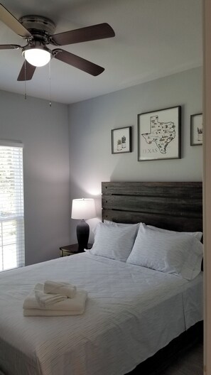 A bedroom with a bed, a ceiling fan, a nightstand with a lamp, and framed artwork on the wall. - Charming 3-bedroom house in marvelous Dallas with AC comfort (Dallas)