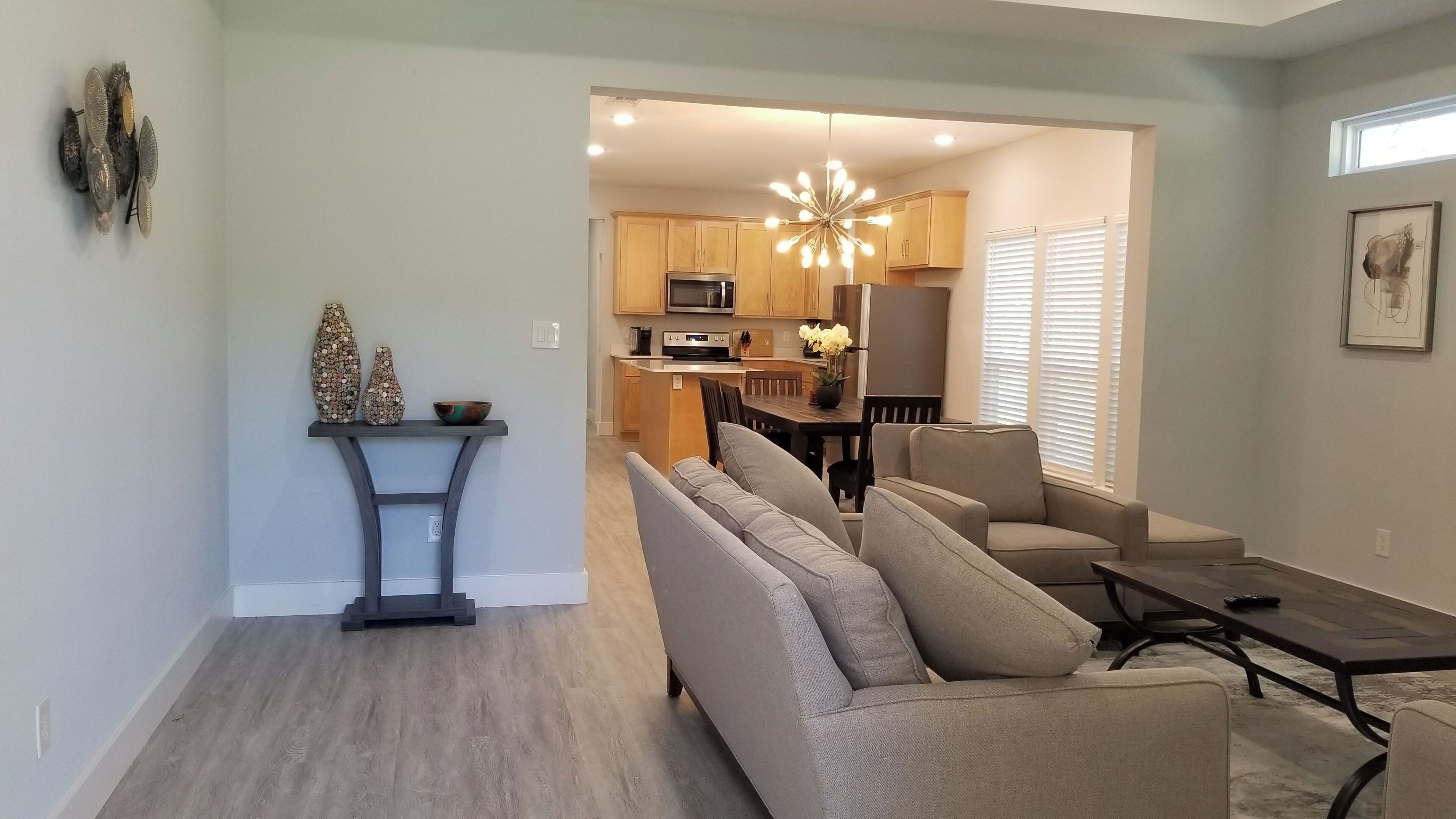 A modern living room with a grey sofa, a dining table, and a kitchen in the background.