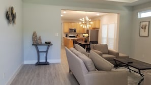 A modern living room with a grey sofa, a dining table, and a kitchen in the background.