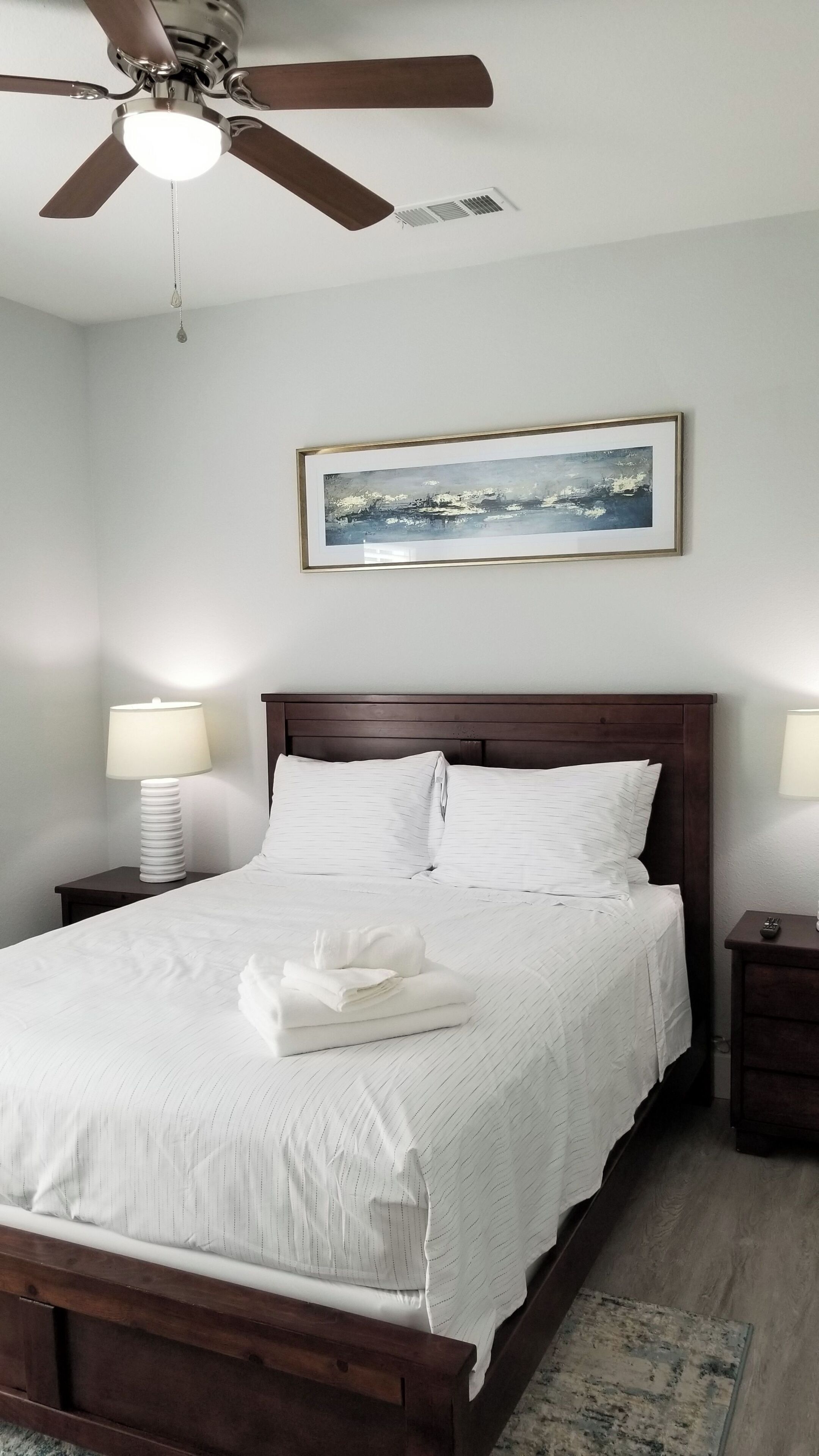 A neatly made bed with white linens, a wooden headboard, and a ceiling fan.
