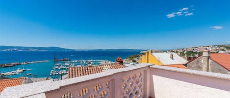 A coastal view with a marina, terracotta-roofed buildings, and a clear blue sky.