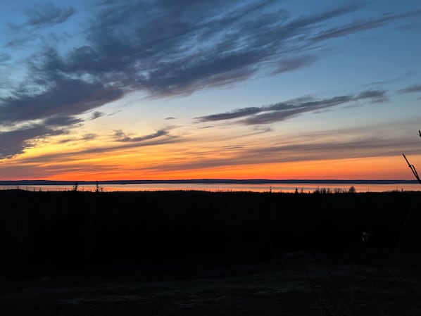 A sunset over a body of water with silhouettes of trees and a distant horizon.