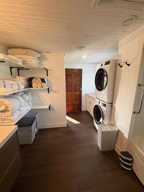 Un cuarto de lavado con lavadora, secadora y estantes con ropa doblada.
