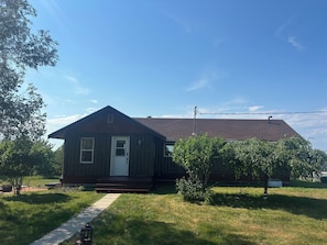 A small, single-story wooden house with a front door, a small porch, and a clear sky.