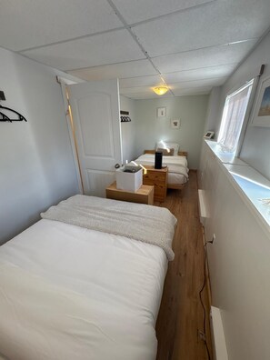 Ein schmales Hotelzimmer mit zwei Betten, einem Nachttisch mit Lampe und einem Fenster mit Blick.