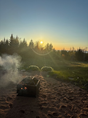 A campfire in a natural setting with trees and a clear sky.
