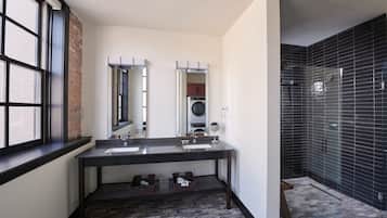 A modern bathroom with two sinks, a large mirror, a built-in washing machine, and a shower area with black tiles.