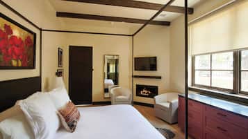A bedroom with a bed, a chair, a TV, a fireplace, and a window.